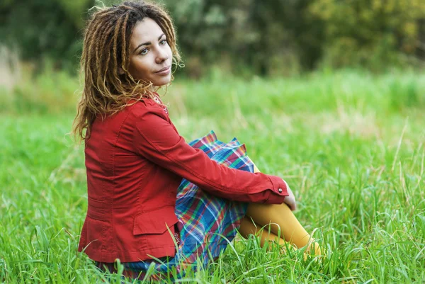 Žena s dredy sedět na trávě — Stock fotografie