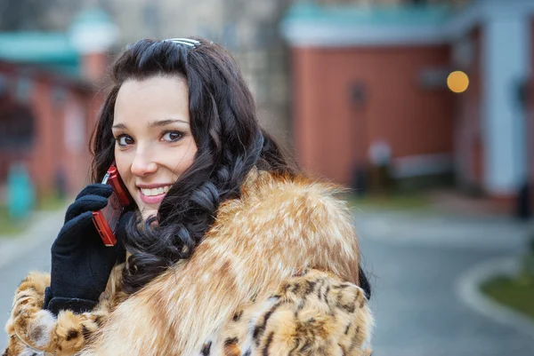 Mulher sorridente em casaco marrom com telefone — Fotografia de Stock
