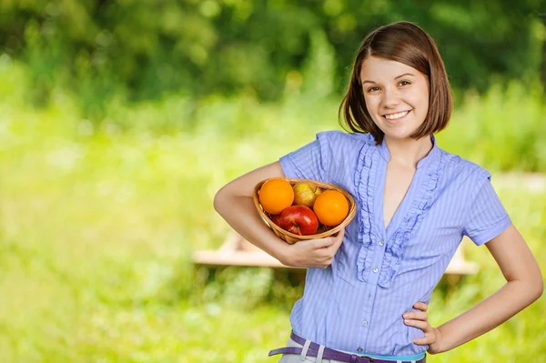 Portrait of young smiling brunette holding basket with fruits — Stock Photo, Image