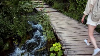 Plitvice Ulusal Parkı 'ndaki tahta köprü boyunca yürüyen şortlu genç yürüyüşçü.