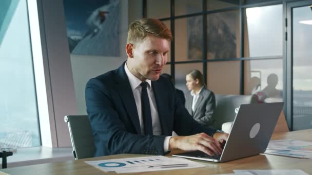 Молодой человек в костюме работает с ноутбуком в офисе. Бизнесмен за столом с ноутбуком — стоковое видео