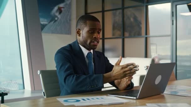 アフリカ系アメリカ人の若い男がオフィスのノートパソコンで働いてる。ビデオ会議を開いてる若い男 — ストック動画