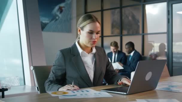 スーツを着た若い女性がオフィスのノートパソコンで働いている。ノートパソコン付きテーブルのビジネスウーマン — ストック動画