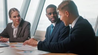 Takım elbiseli gençler iş toplantısında iletişim kuruyor. İş adamları soruları tartışıyor ve kurumsal verileri analiz ediyorlar