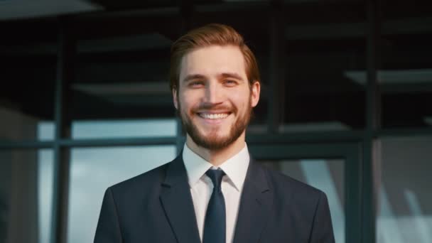Jonge zakenman lachend en kijkend naar de camera. Jongeman in een pak op kantoor — Stockvideo