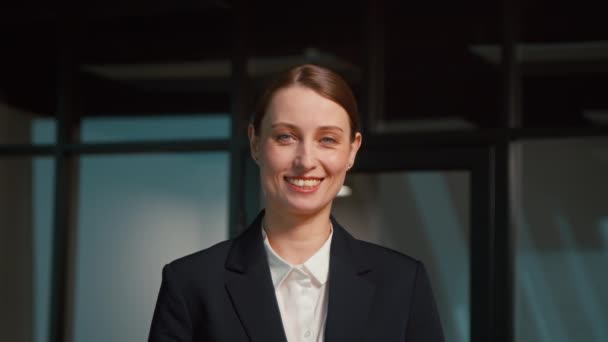 Jonge zakenvrouw glimlachend en kijkend naar de camera. Jonge vrouw in een pak op kantoor — Stockvideo