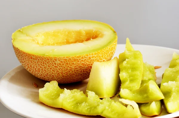 La mitad de melón maduro se pela en un plato, naturaleza muerta —  Fotos de Stock