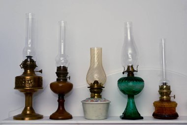 Tarafsız bir arkaplanda rafta duran beş eski gazyağı lambası.