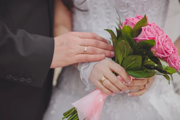 Mãos e anéis no buquê de casamento — Fotografia de Stock