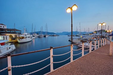 Marmaris marinası Türkiye 'nin Mugla kentinin güzel günbatımı şehir merkezi manzarası. Şehir ışıkları yat limanında, denizde, şehirde, dağlarda, yatlarda ve yelkenlilerde..