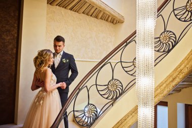 Bir çift yeni evli çift lüks bir iç mekanda merdivenlerde dikiliyorlar..