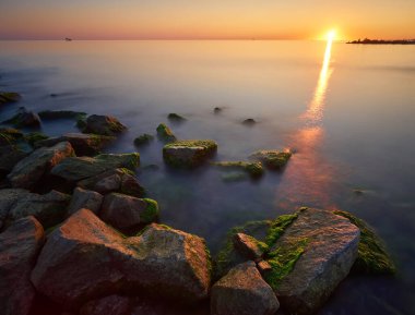 Gün batımında deniz manzarası. Taşlar ve kayalarla dolu uzun bir kepenk..