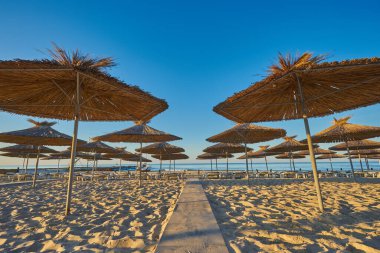 Sahilde şafak söktü. Güneş ve şemsiyeler yükselen güneşin ışınlarında. İnsanlar olmadan plaj.