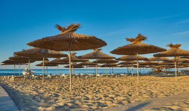 Yaz tatili için cennet gibi bir tropik tatil beldesindeki kumsalda Thatched plaj şemsiyeleri ve şezlongları