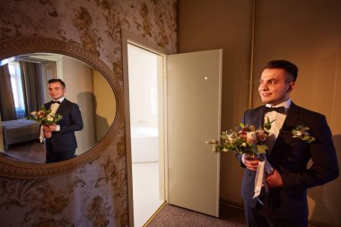 Şık damat büyük bir pencerenin yanında duruyor. Stüdyoda genç bir adamın düğün portresi. Damadın sabahı. Şık bir erkeğin düğün portresi. Boşluğu kopyala.