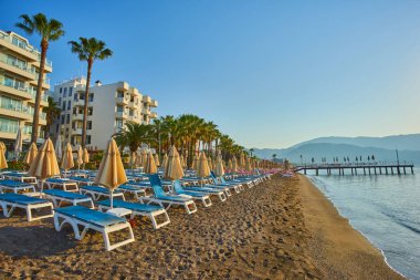 Bulutsuz havada deniz kıyısında akşam kumsalı. Şemsiyeli ve güneşli kumlu bir sahilde gün batımı