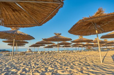 Deniz kıyısı, şemsiyeli kumsal ve şafakta deniz ve gökyüzünün arka planında güneşlik.