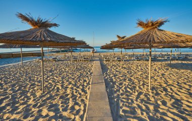 Yaz tatili için cennet gibi bir tropik tatil beldesindeki kumsalda Thatched plaj şemsiyeleri ve şezlongları