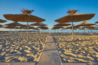 Sahilde şafak söktü. Güneş ve şemsiyeler yükselen güneşin ışınlarında. İnsanlar olmadan plaj.