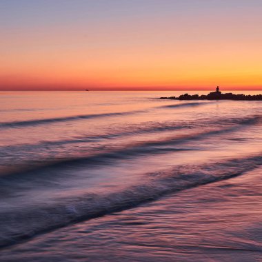 Plajda gün batımında gökyüzü arka planında yumuşak deniz dalgaları ve kabarcıklar.