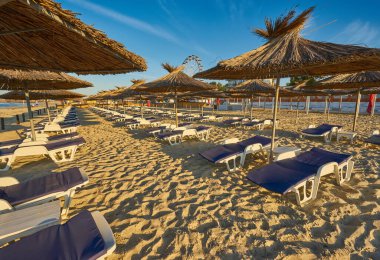 Yaz tatili için cennet gibi bir tropik tatil beldesindeki kumsalda Thatched plaj şemsiyeleri ve şezlongları