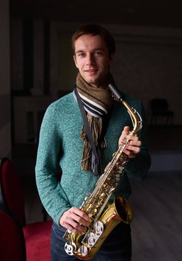 Genç müzik sanatçısı Jazzman elinde saksafon tutuyor. Konser salonunun karanlık odası, pencereden gelen ışıkla aydınlanıyor.