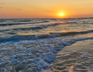 Plajda gün batımında gökyüzü arka planında yumuşak deniz dalgaları ve kabarcıklar.