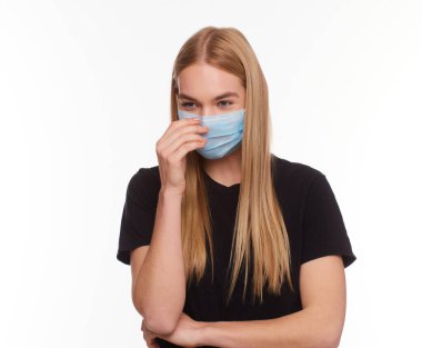 Sarışın, tıbbi maske takan genç bir kadın elleriyle düzeltiyor izole edilmiş beyaz arka planı.