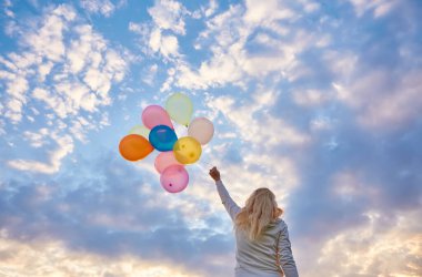 Gün batımında çayırlarda renkli balonlarla koşan genç bir kadın.