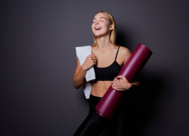 Siyah arka planda yoga minderi ve havlusu olan güzel bir kadın. Metin için boşluk