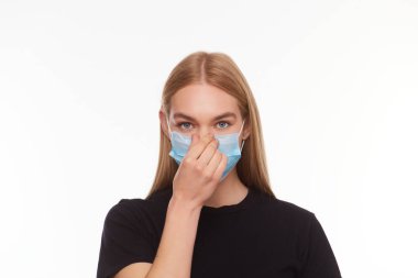 Sarışın, tıbbi maske takan genç bir kadın elleriyle düzeltiyor izole edilmiş beyaz arka planı.