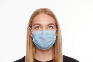 Tıbbi maskeli bir kadın yüzü beyaz bir arkaplana bakıyor.