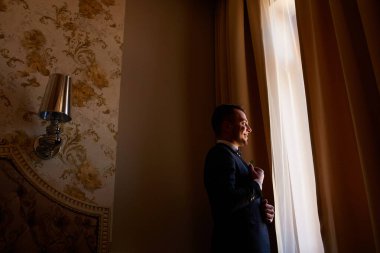 Şık damat büyük bir pencerenin yanında duruyor. Stüdyoda genç bir adamın düğün portresi. Damadın sabahı. Şık bir erkeğin düğün portresi. Boşluğu kopyala.