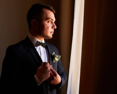 Beyaz gömlekli genç adam pencerenin yanındaki kol düğmelerini takıyor. İş portresi. Damat gelinle buluşacak. Düğün için. İş adamı. Nişanlı.