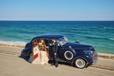 Güneşli bir günde plajda arabanın yanında kucaklaşan genç ve güzel bir çift.