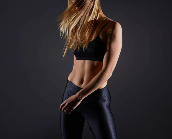 stock image Athletic young blonde girl in sportswear shows muscles on a black background. Great athletic female body