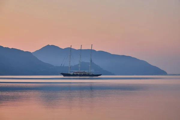 穏やかな海での日の出を反映した山と孤独なモーターボートトルコのマーマリス — ストック写真