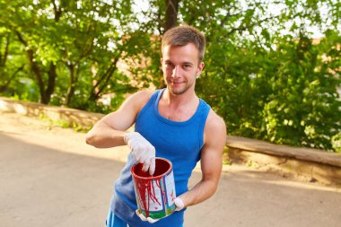 Adam duvarı parlak renklerle boyuyor, elinde bir kutu boya tutuyor, sokakta.