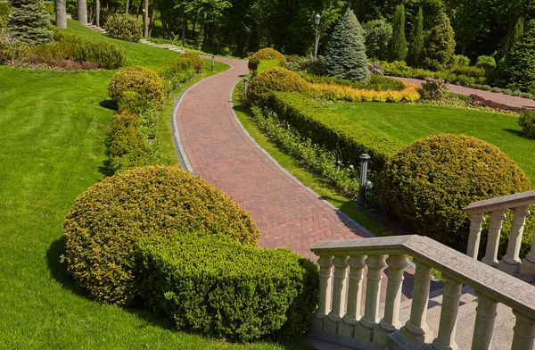 公园背景上的楼梯上有石栏杆 栏杆和铁灯 有豪华的景观设计步行路径 可以走 有绿色的草坪和各种灌木丛 — 图库照片