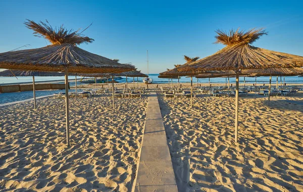 Yaz tatili için cennet gibi bir tropik tatil beldesindeki kumsalda Thatched plaj şemsiyeleri ve şezlongları