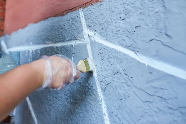 Eldeki fırça duvarı beyaza boyuyor, binanın ön cephesini boyuyor.