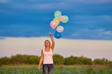 Gün batımında çayırlarda renkli balonlarla koşan genç bir kadın.