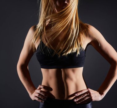 Spor salonunun siyah duvarında duran sarışın kız. Vücut geliştirme ve saç süpürme