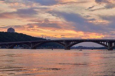Kyiv şehrindeki ilk metro köprüsünün üzerindeki Dinyeper Nehri 'nin sağ kıyısından görüntü. Akşam fotoğrafı, şehir ışıkları nehire yansıyor.