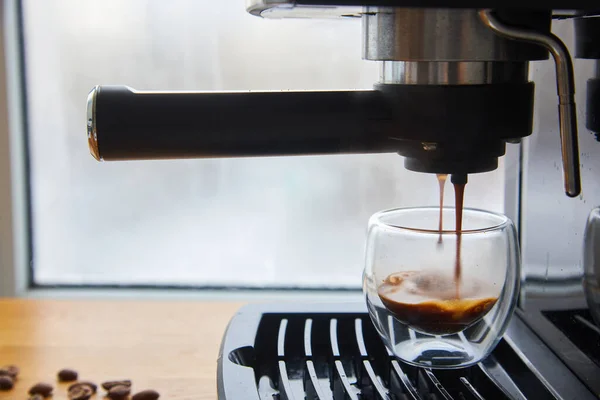 Making fresh coffee going out from a coffee espresso machine. Making espresso in glass transparent coffee cup.