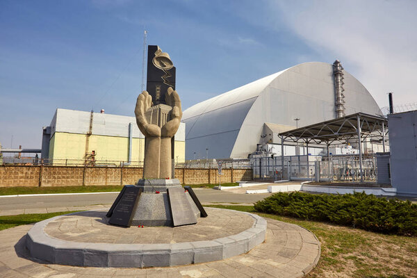 PRIPYAT, UKRAINE - April 25 2019: Monument to the Chernobyl Liquidators and fourth reactor without enclosing sarcophagus. Chornobyl Nuclear Power Plant - ChNPP