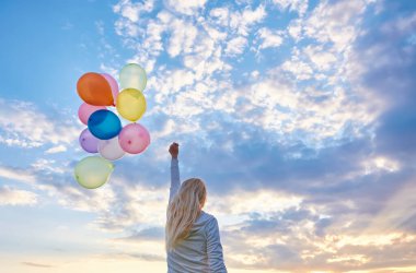 Gün batımında çayırlarda renkli balonlarla koşan genç bir kadın.