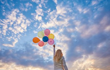 Günbatımında yeşil sahada çalışan balonlar ile mutlu bir kadın.