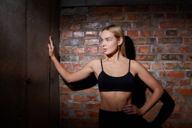 Spor ve yoga yaşam tarzı konsepti. Spor kıyafetleri giymiş genç ve güzel bir kadın tuğla duvara karşı poz veriyor..