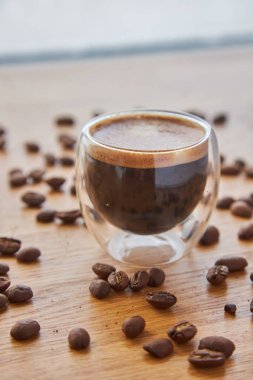 Şeffaf bir fincanda Espresso, ahşap bir masanın üzerinde duruyor, arka planda kahve çekirdekleri ile çevrili.